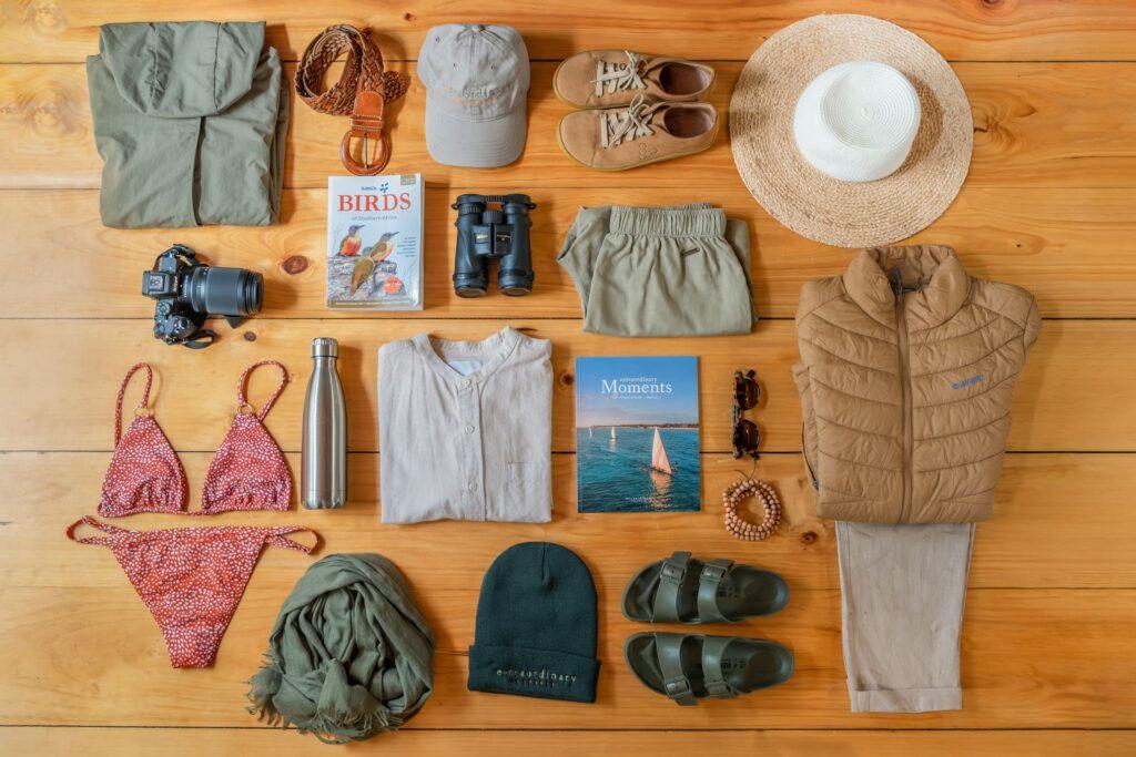 Safari packing flat lay with khaki clothing, sun hat, binoculars, camera, bird guide and swimwear