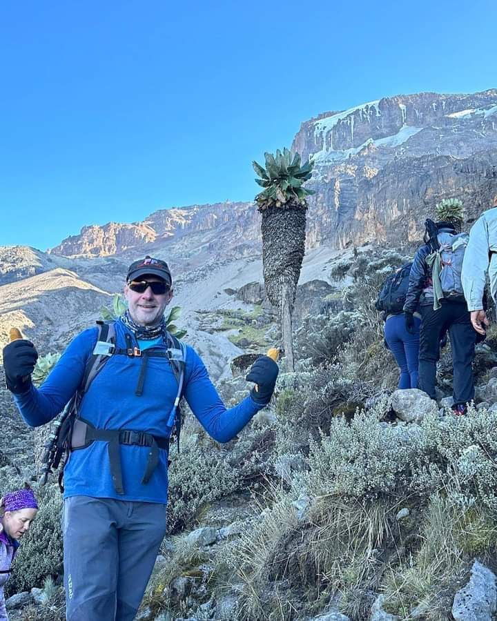 Trekker celebrating beside a giant groundsel on the Northern Circuit