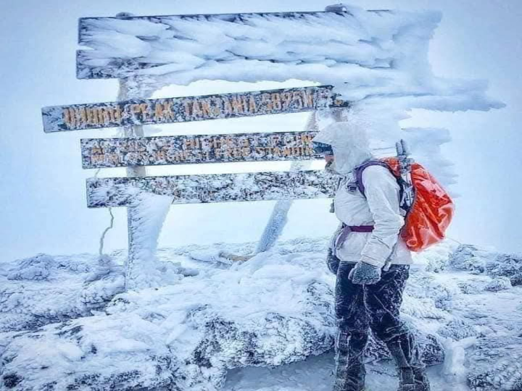 Climber at the frozen Uhuru Peak signboard in heavy rime ice